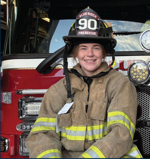 Emmaleen Regan leaning against a fire truck in fire gear